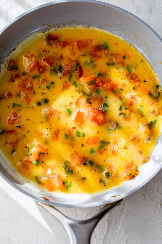 Eggs added to skillet with tomatoes and scallions
