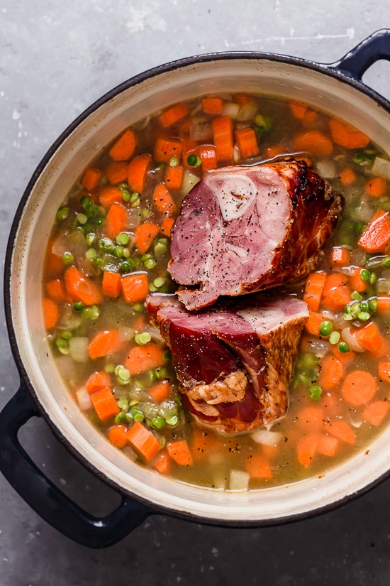 A dutch oven with ingredients for split pea soup with ham.