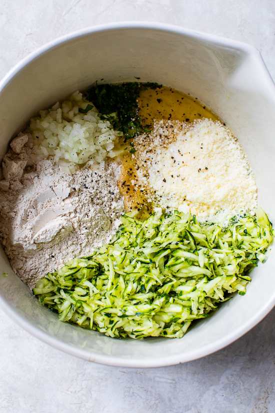 grates zucchini, parmesan cheese, bisquick, and egg in a bowl.