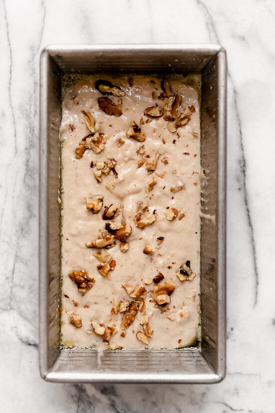 This delicious banana bread is be made with ripe mashed bananas, nuts, and spices. It's made healthier with less butter, oil and sugar. Batter for banana nut bread ready to bake in a pan.