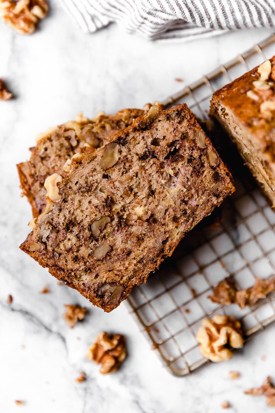 This delicious banana bread is be made with ripe mashed bananas, nuts, and spices. It's made healthier with less butter, oil and sugar. Banana nut bread slices stacked on a wire rack.