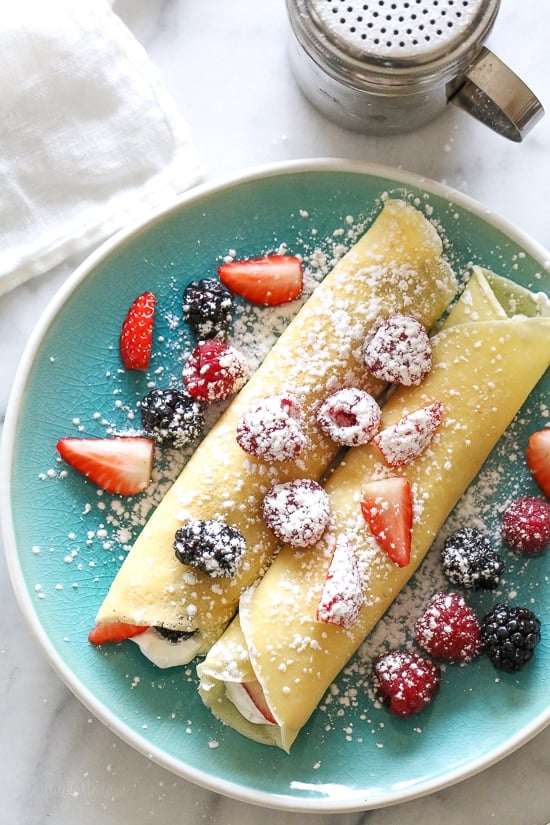 Homemade crepes with whipped cream and fresh berries on a blue plate