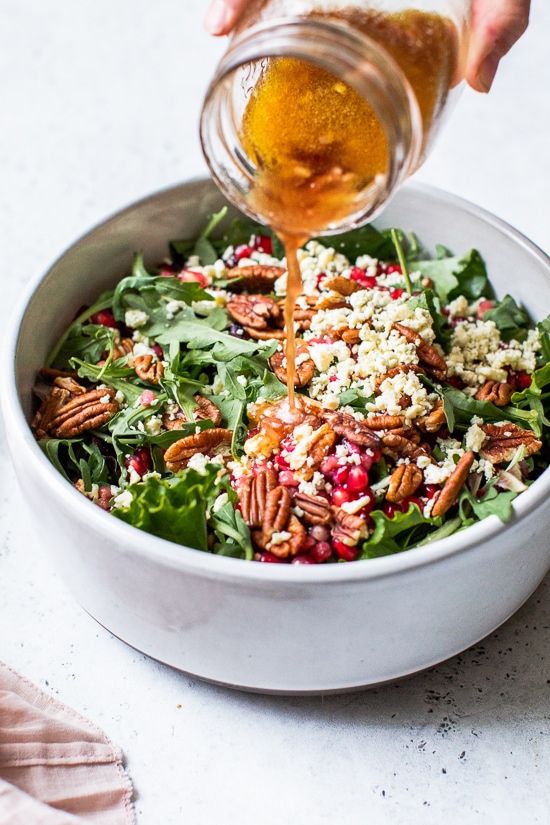 Pouring pomegranate vinaigrette over salad.
