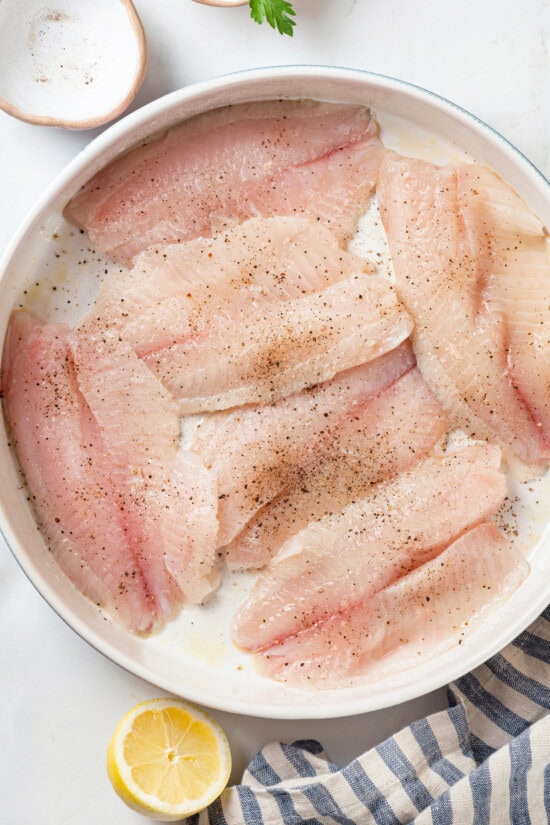 This simple baked tilapia recipe is finished with a garlicky lemon butter sauce and parsley, making it a delicious and light weeknight dinner! Tilapia in baking dish