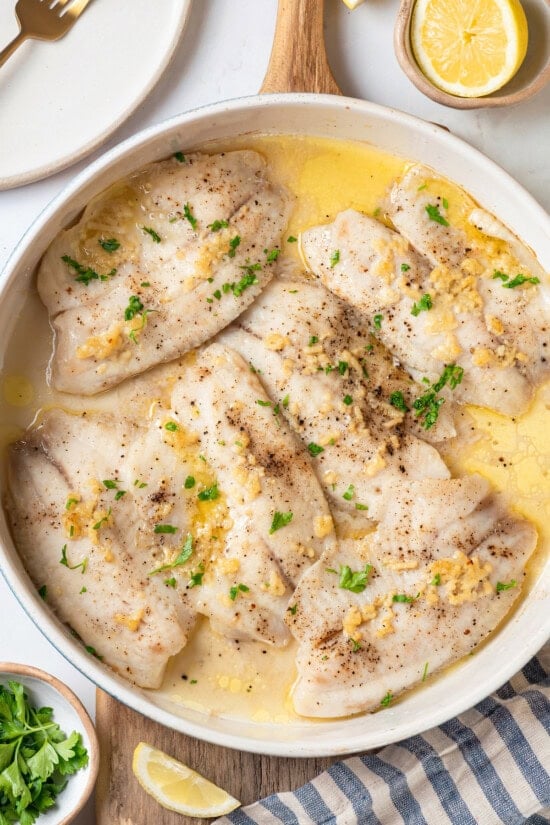 This simple baked tilapia recipe is finished with a garlicky lemon butter sauce and parsley, making it a delicious and light weeknight dinner! Overhead view of baked tilapia in skillet