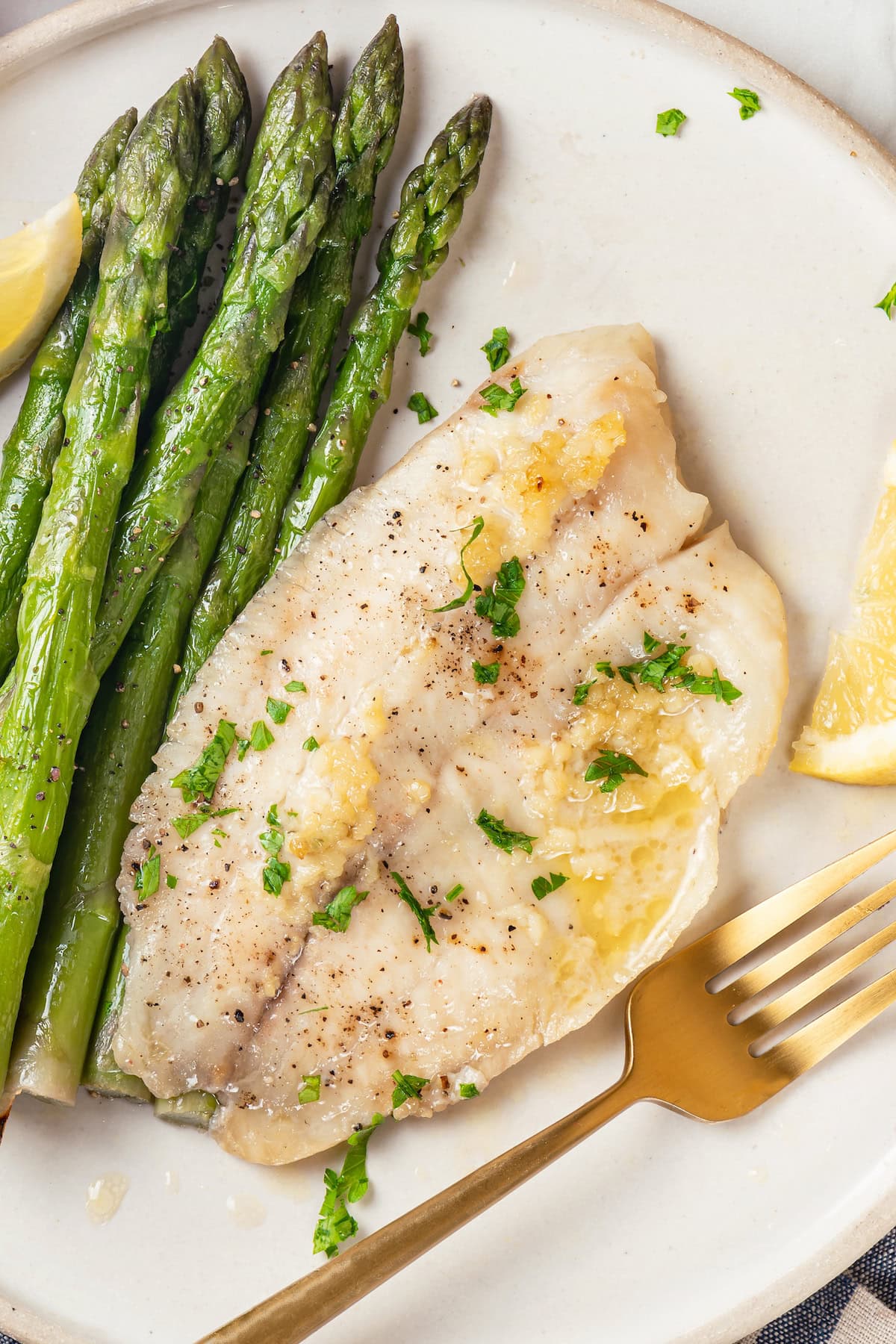 This simple baked tilapia recipe is finished with a garlicky lemon butter sauce and parsley, making it a delicious and light weeknight dinner! Easy baked tilapia on plate with asparagus