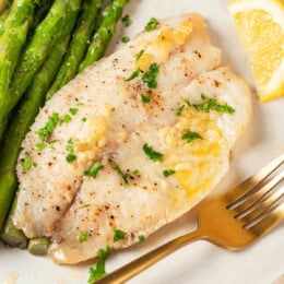Closeup of baked tilapia on plate with asparagus