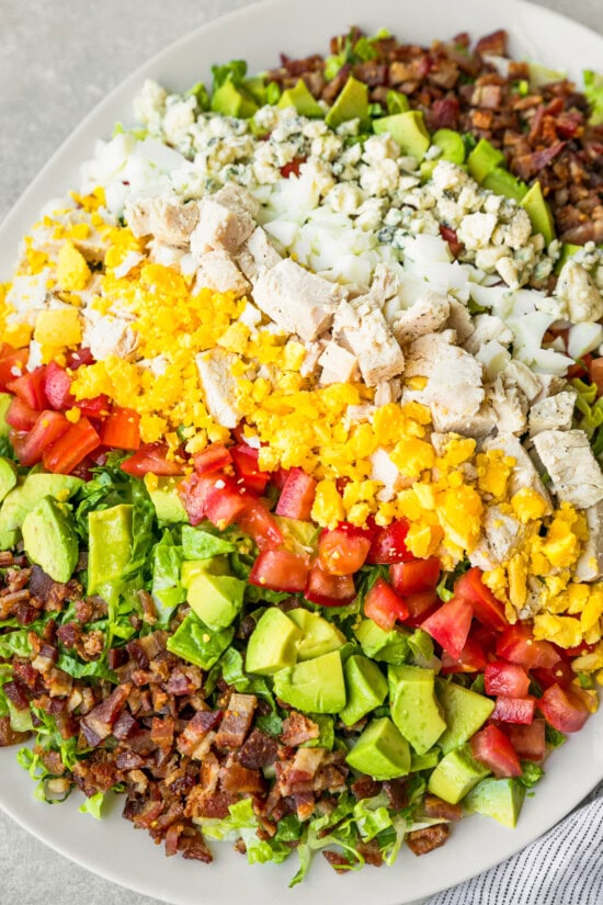 Layers of hard boiled eggs, bacon, blue cheese, tomatoes and avocado make up this classic Cobb salad recipe. It's the perfect lunch salad! Easy Cobb salad recipe on serving plate