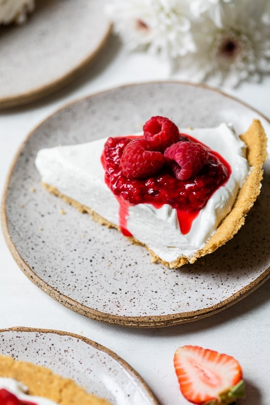 Slice of creamy no-bake cheesecake topped with macerated and fresh raspberries