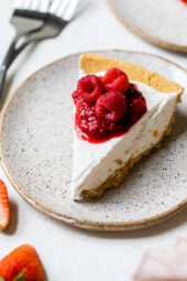 Slice of no-bake cheesecake on plate with macerated and fresh raspberries on top