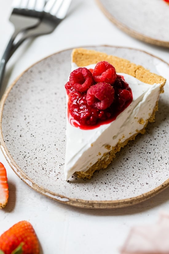 Slice of no-bake cheesecake on plate with macerated and fresh raspberries on top