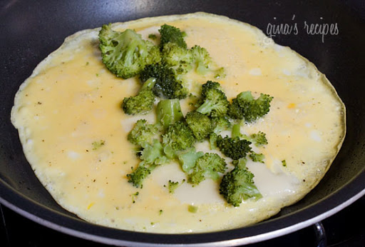 An open omelet with broccoli and cheese in a skillet