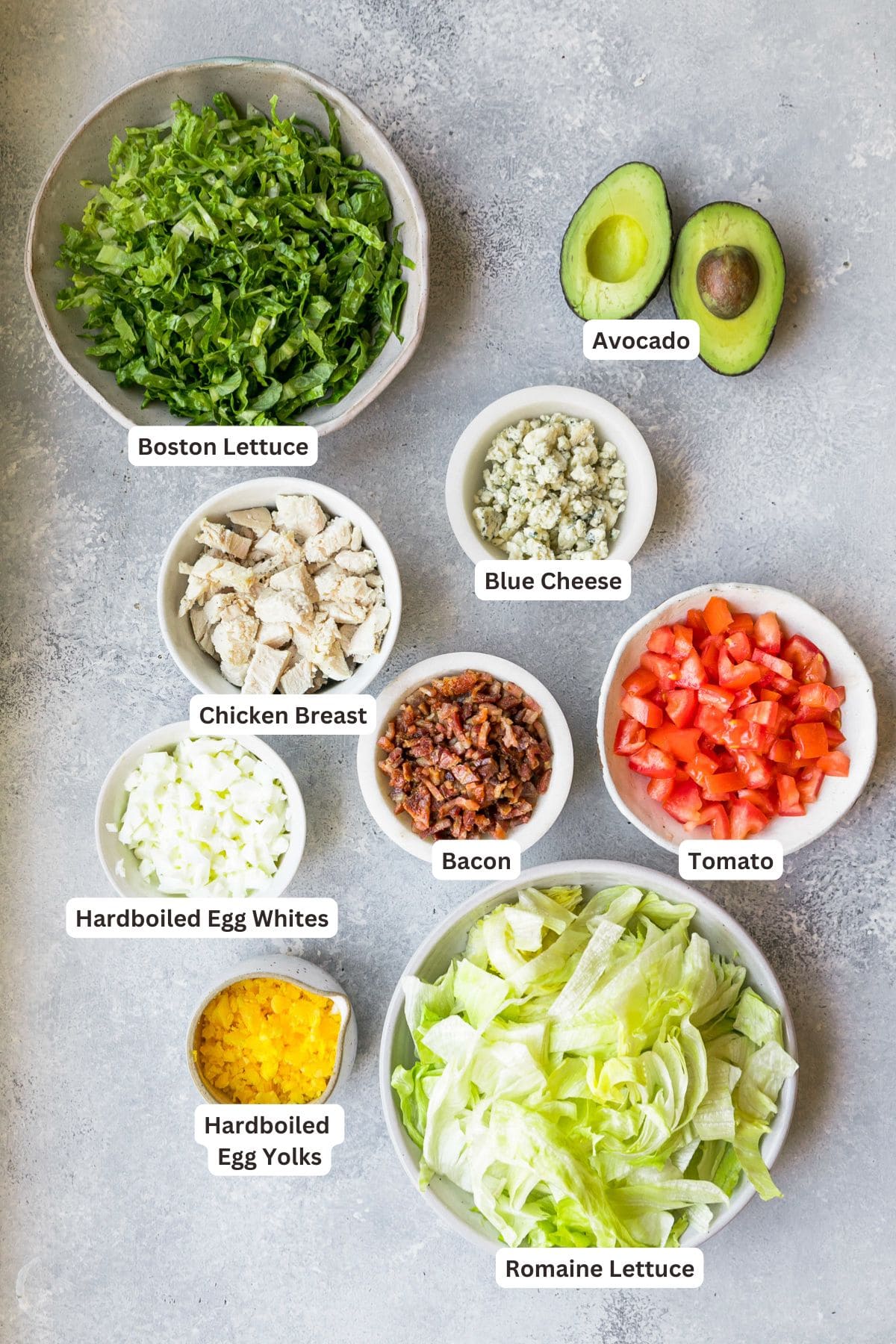 Ingredients for cobb salad in white bowls on a marble background.