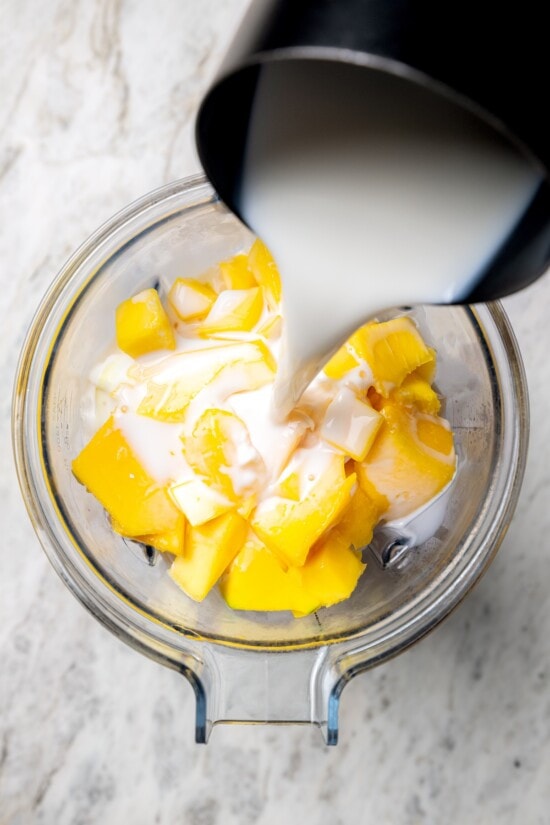Pouring milk into blender with fresh mango cubes