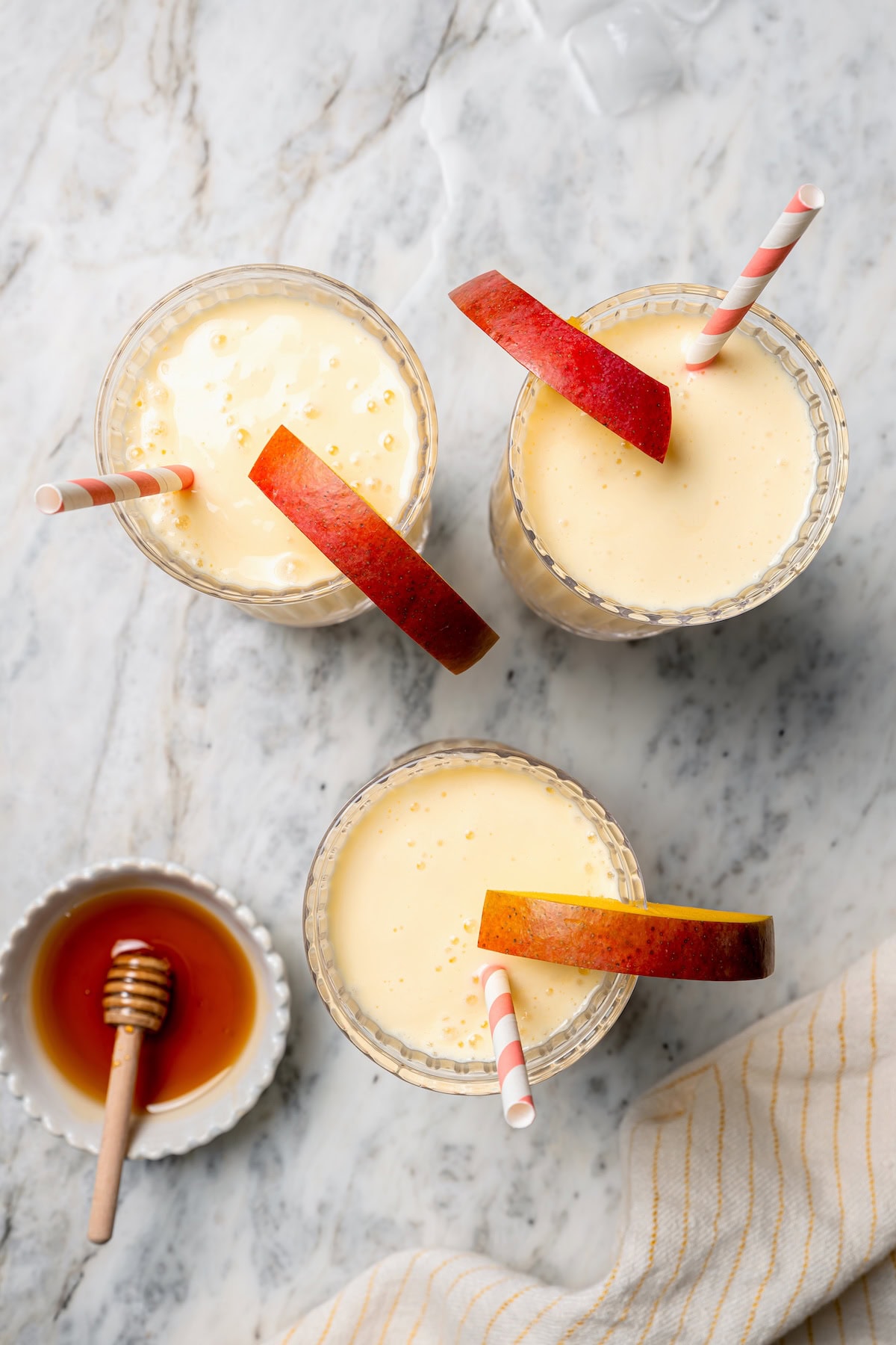 Overhead view of 3 glasses of mango lassi and bowl of honey with dipper
