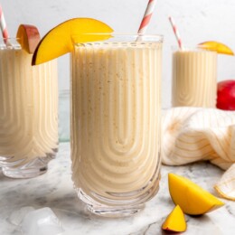 3 homemade mango lassis in glasses with mango slices on rim for garnish