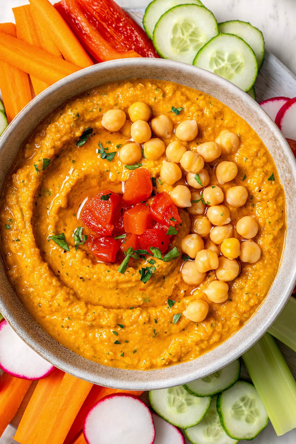 Smoky bell peppers add so much flavor to this roasted red pepper hummus recipe! Pair it with your favorite veggies for a healthy snack. Overhead view of roasted red pepper hummus in bowl surrounded by fresh veggies