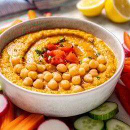Bowl of roasted red bell pepper hummus garnished with peppers and chickpeas