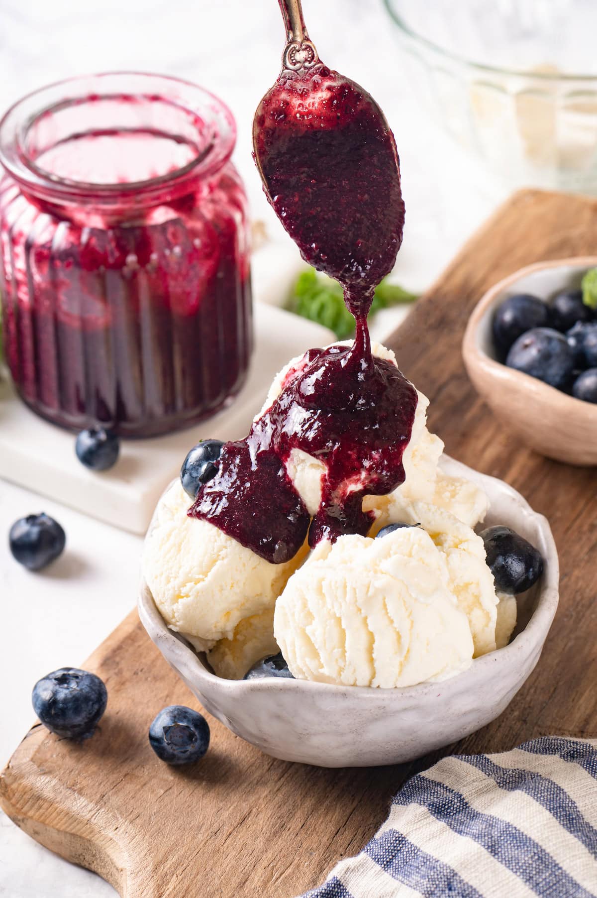This easy blueberry compote recipe is a 3-ingredient fruit topping perfect for serving over ice cream, yogurt, and more. So summery! Spooning blueberry fruit compote onto bowl of vanilla ice cream