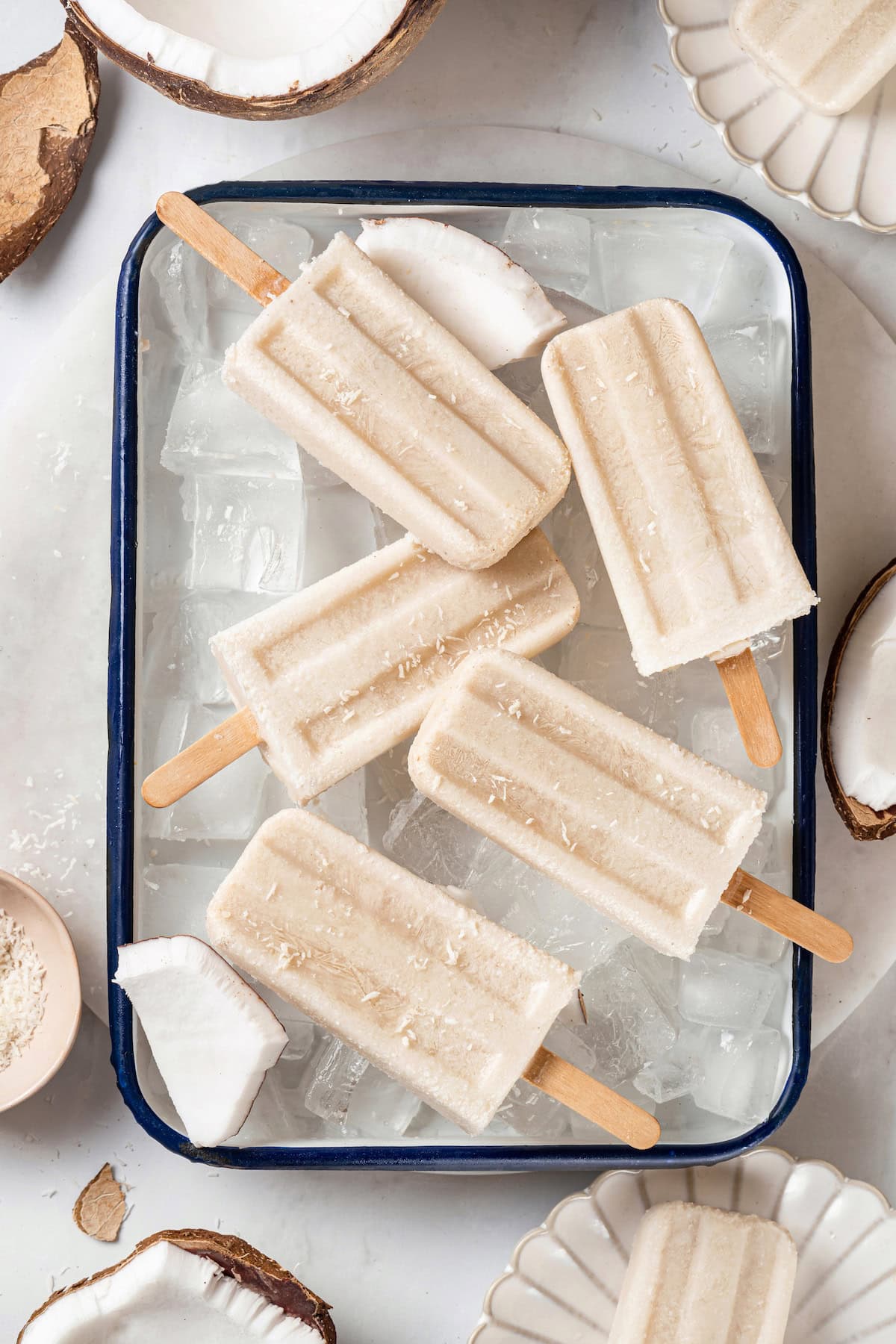 These homemade coconut popsicles are rich, creamy, and super simple to make! They’re the perfect summertime refresher. Overhead view of coconut cream pops in pan of ice