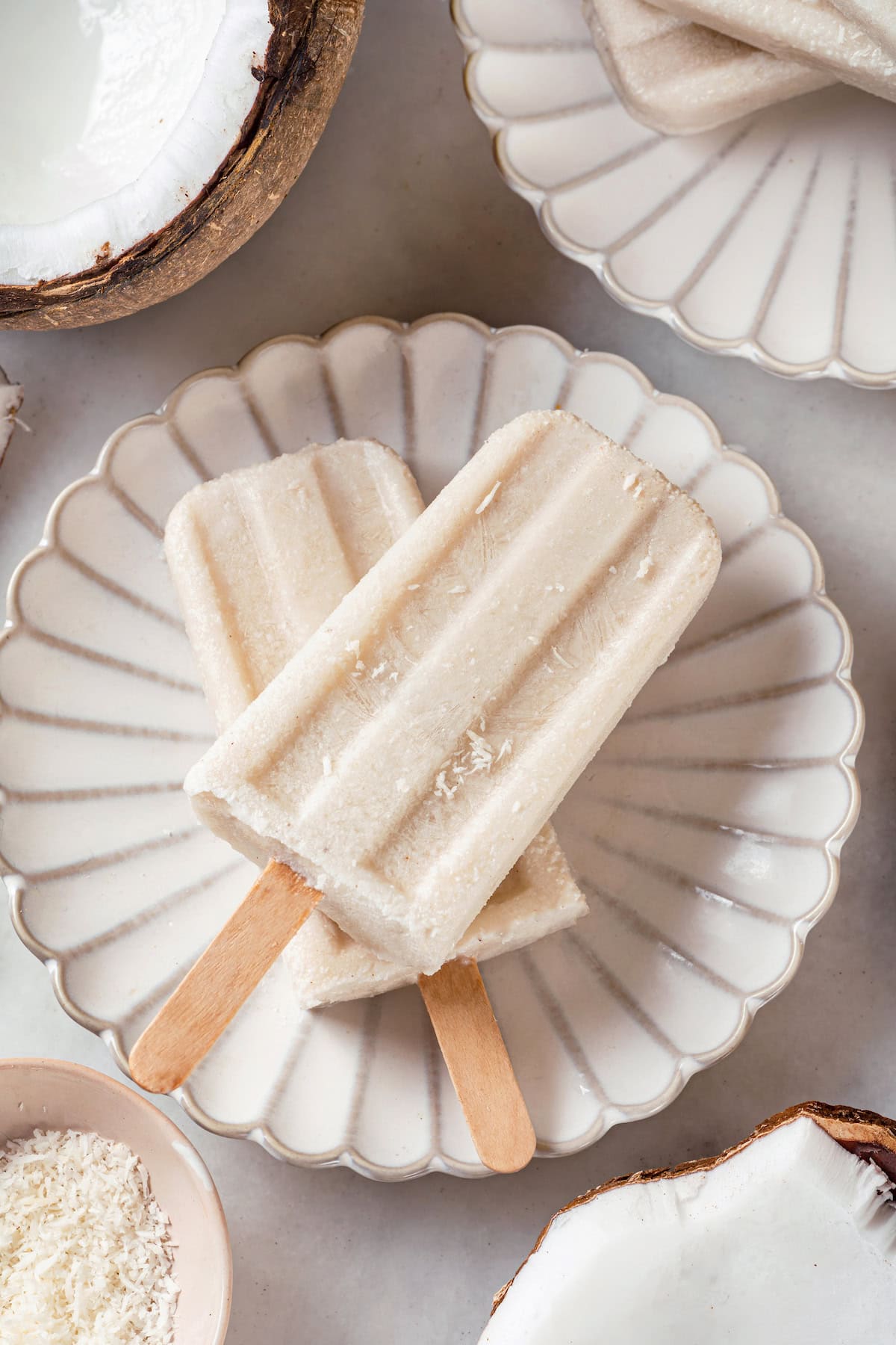 These homemade coconut popsicles are rich, creamy, and super simple to make! They’re the perfect summertime refresher. Two coconut popsicles set on plate