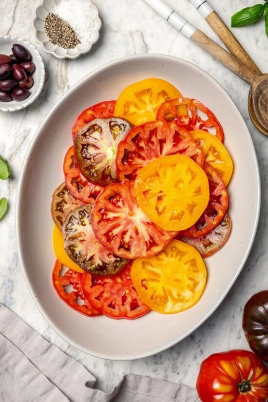 With juicy, ripe tomatoes, red onion, briny olives and fresh basil, this easy heirloom tomato salad recipe is absolutely packed with flavor! Overhead view of sliced heirloom tomatoes on platter