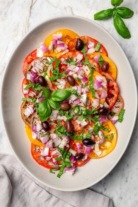 With juicy, ripe tomatoes, red onion, briny olives and fresh basil, this easy heirloom tomato salad recipe is absolutely packed with flavor! Overhead view of heirloom tomato salad with basil and kalamata olives