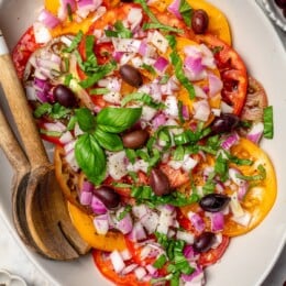 Overhead view of heirloom tomato salad on platter with serving spoons