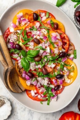 Overhead view of heirloom tomato salad on platter with serving spoons