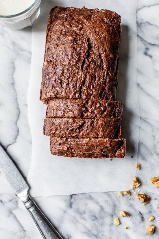 This Chocolate Zucchini Bread is so rich and delicious, no one will guess that it's secretly healthy! Add walnuts for crunch in every bite. Overhead view of sliced Chocolate Zucchini Bread loaf on white marble
