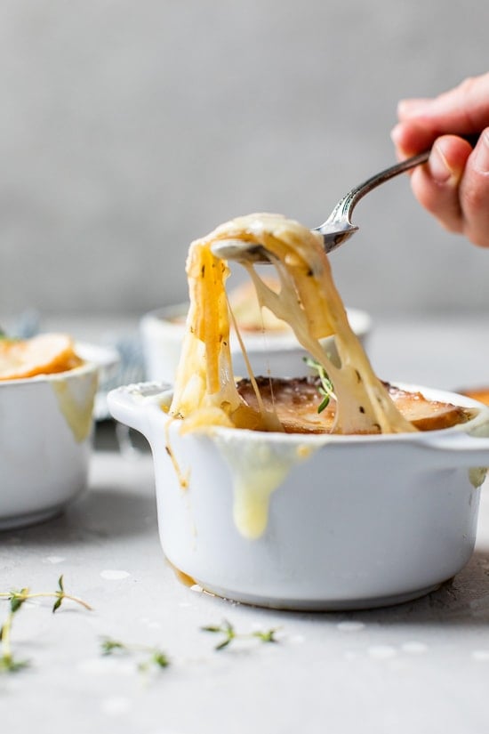 This lightened-up French onion soup recipe is just as delicious as the original, with beefy broth, caramelized onions, and melty cheese! A spoonful of cheesy French onion soup being lifted from a ramekin.