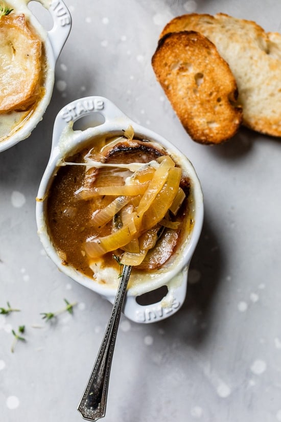 This lightened-up French onion soup recipe is just as delicious as the original, with beefy broth, caramelized onions, and melty cheese! Overhead view of a spoon resting in a bowl of French onion soup.