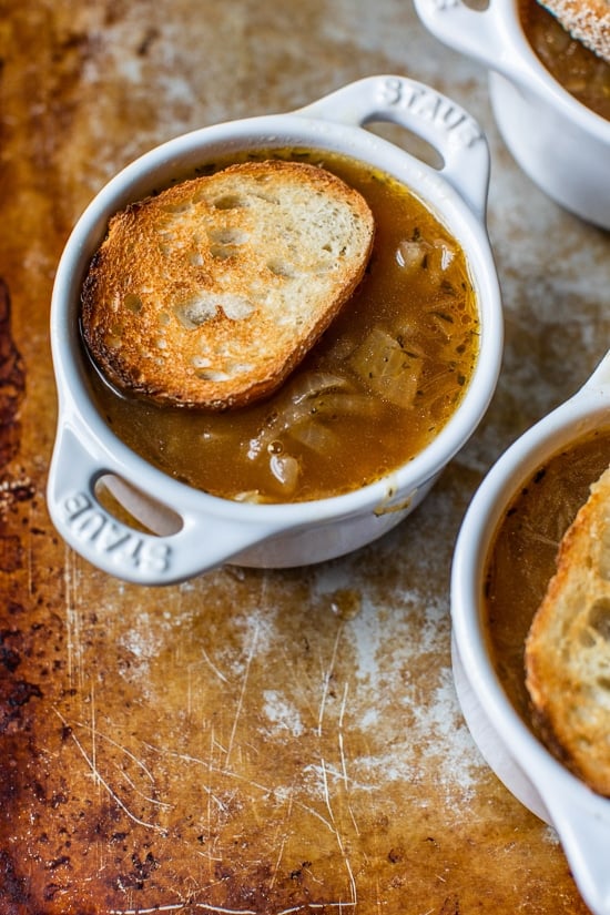 This lightened-up French onion soup recipe is just as delicious as the original, with beefy broth, caramelized onions, and melty cheese! French onion soup topped with a slice of toasted bread in a ramekin.