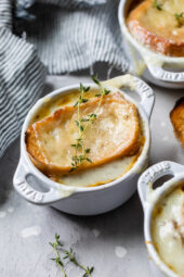 French onion soup in ramekins topped with toast and melted cheese, garnished with thyme sprigs.