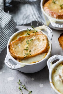 French onion soup in ramekins topped with toast and melted cheese, garnished with thyme sprigs.