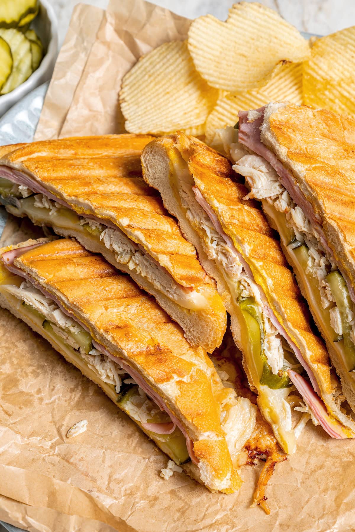 This turkey Cuban sandwich is an easy way to put those Thanksgiving leftovers to use, and my lightened up recipe won’t weigh you down either! 4 turkey Cuban sandwiches on parchment paper with chips