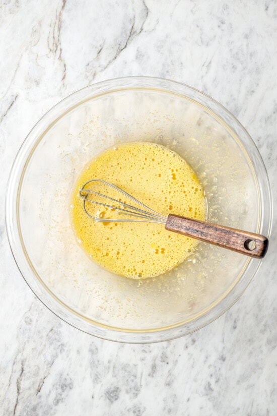 This easy lightened up homemade eggnog recipe comes together quickly and it’s so much tastier than store-bought. Creamy and delicious! Egg and sugar mixture in bowl with whisk