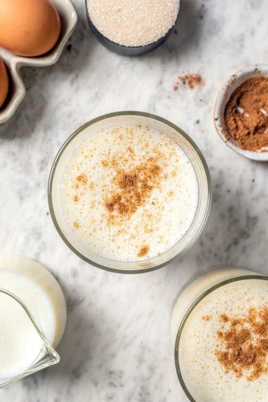This easy lightened up homemade eggnog recipe comes together quickly and it’s so much tastier than store-bought. Creamy and delicious! Overhead view of homemade eggnog in glass with grated nutmeg on top