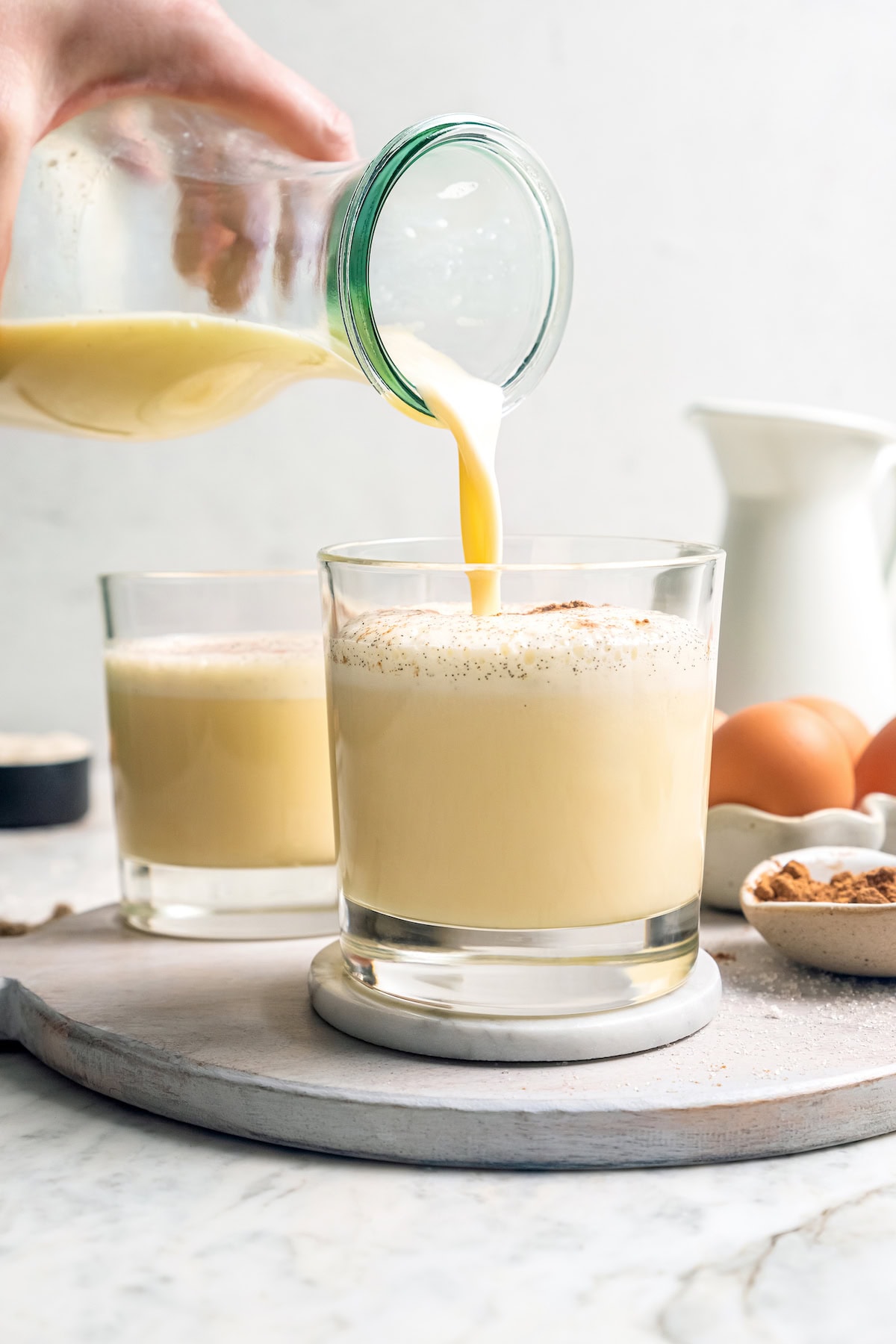 This easy lightened up homemade eggnog recipe comes together quickly and it’s so much tastier than store-bought. Creamy and delicious! Pouring homemade eggnog into glass