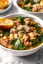 Spoon in bowl of white bean soup with kale and sausage.