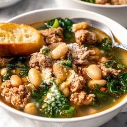 Spoon in bowl of white bean soup with kale and sausage.