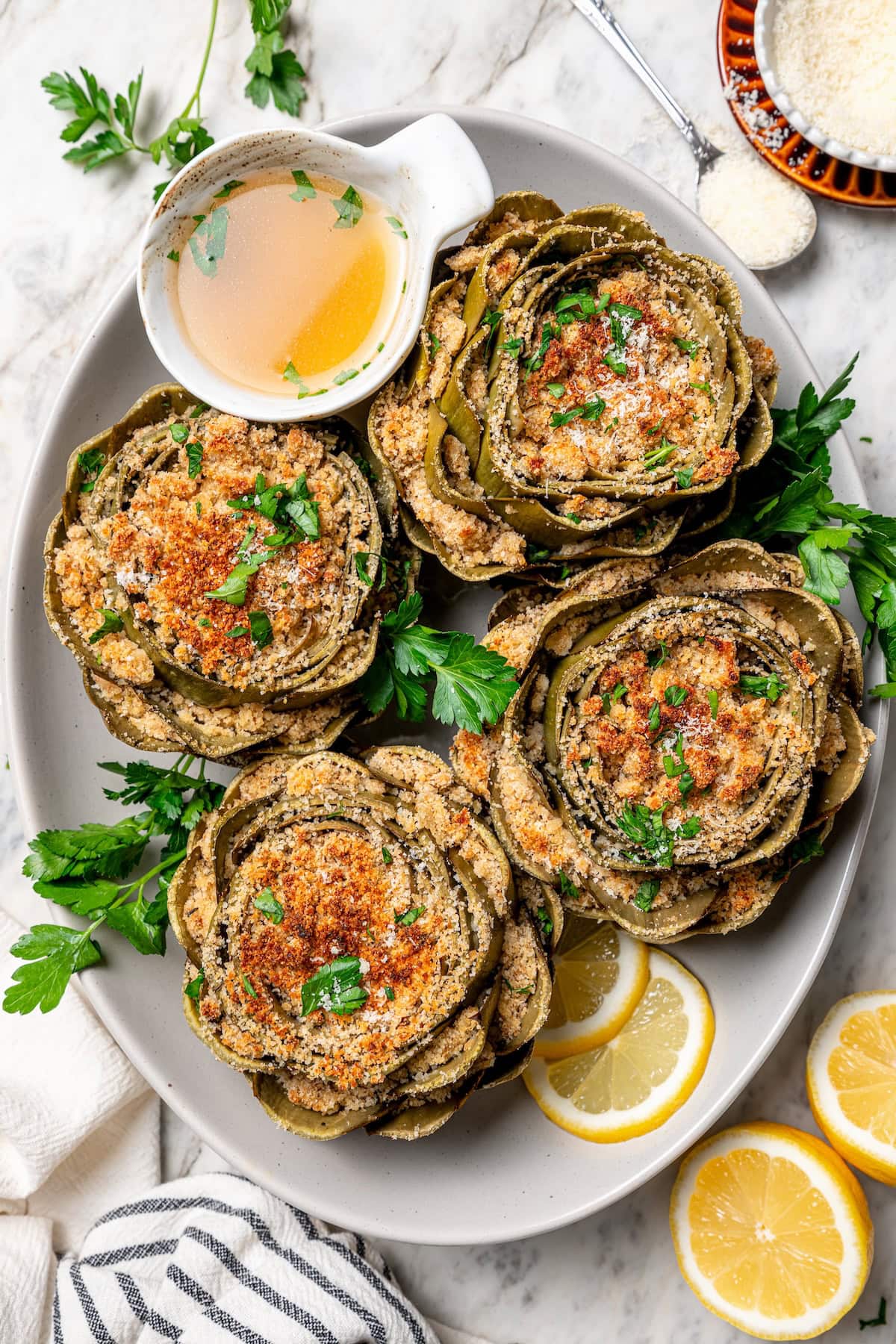 Stuffed artichokes are a classic Italian dish made with crispy, cheesy breadcrumbs. My version is a bit lighter but just as delicious! Overhead view of stuffed artichokes on platter with lemon wheels