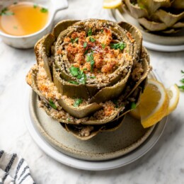 Stuffed artichoke on plate with lemon slices