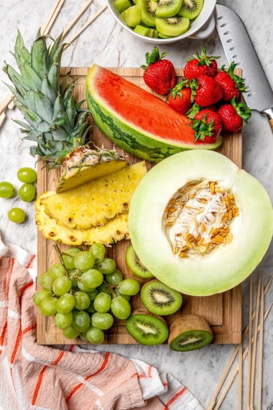 Fruit kabobs are the easiest summer dessert! Made with a rainbow of fruit threaded onto skewers, they’re perfect with a creamy fruit dip. Overhead view of fresh fruit on cutting board