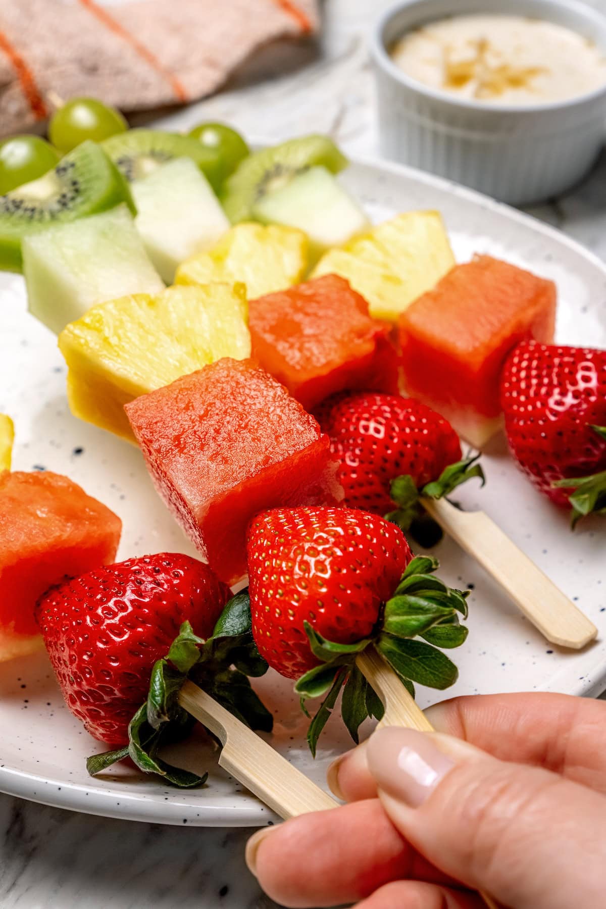 Fruit kabobs are the easiest summer dessert! Made with a rainbow of fruit threaded onto skewers, they’re perfect with a creamy fruit dip. Hand holding fruit kabob on wooden skewer