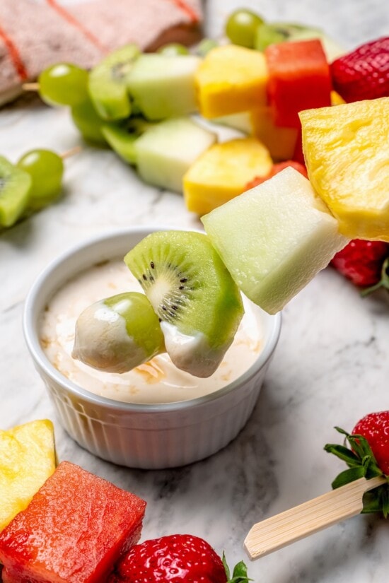 Fruit kabobs are the easiest summer dessert! Made with a rainbow of fruit threaded onto skewers, they’re perfect with a creamy fruit dip. Dipping fruit kabob in bowl of dip