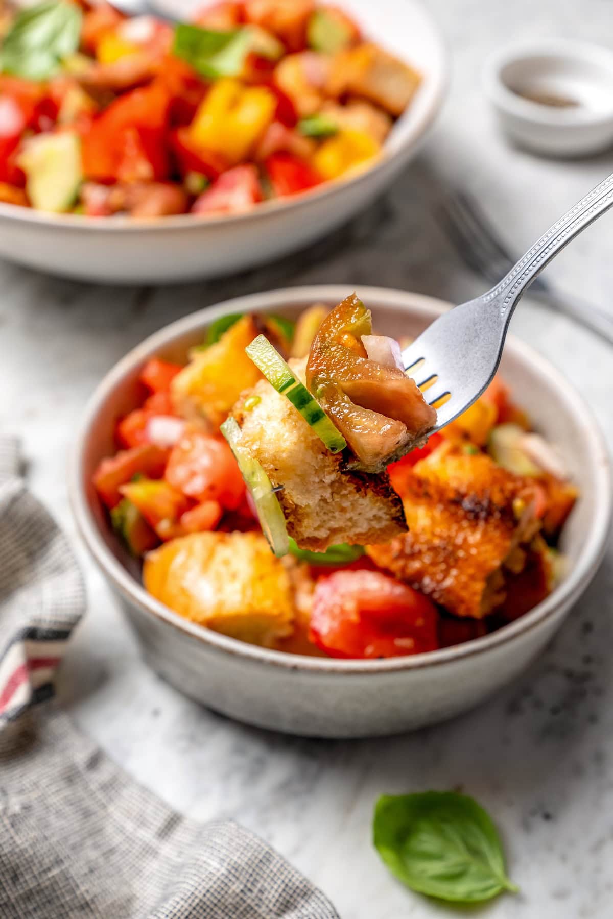 With juicy heirloom tomatoes, crisp cubes of bread, cucumber, and fresh basil, this panzanella recipe is a dish you’ll find yourself making all summer long. Serve it as a side or as a light meal. Forkful of panzanella held over bowl