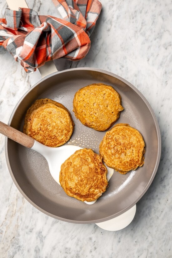 This lightened up version of pumpkin pancakes is also extra fluffy! You'll love the cozy fall flavor in this easy, healthier pancake recipe. Overhead view of spatula flipping pumpkin pancake in skillet