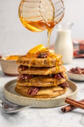 Pouring syrup over stack of pumpkin pancakes on plate