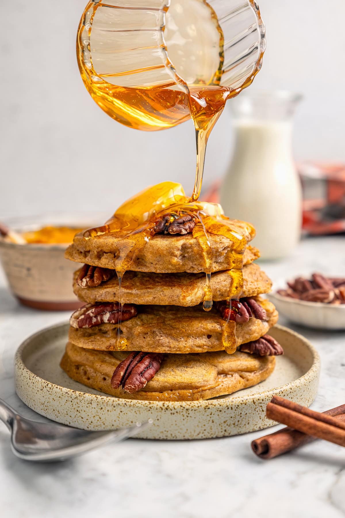 Pouring syrup over stack of pumpkin pancakes on plate